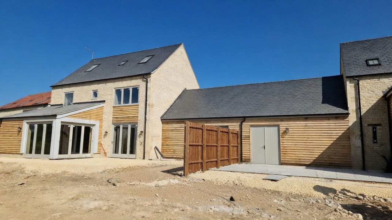 Newly built courtyard of barn-style stone dwellings with coursed limestone walling, cedar cladding and slate roofs nearing completion
