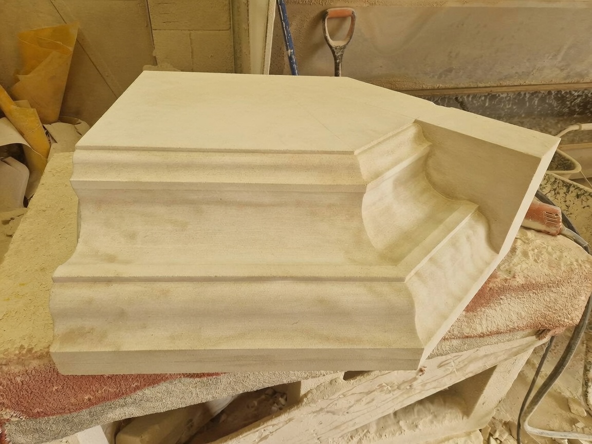 Hand-worked limestone cornice block with stepped mouldings and a mitred return, resting on the banker in the masonry workshop