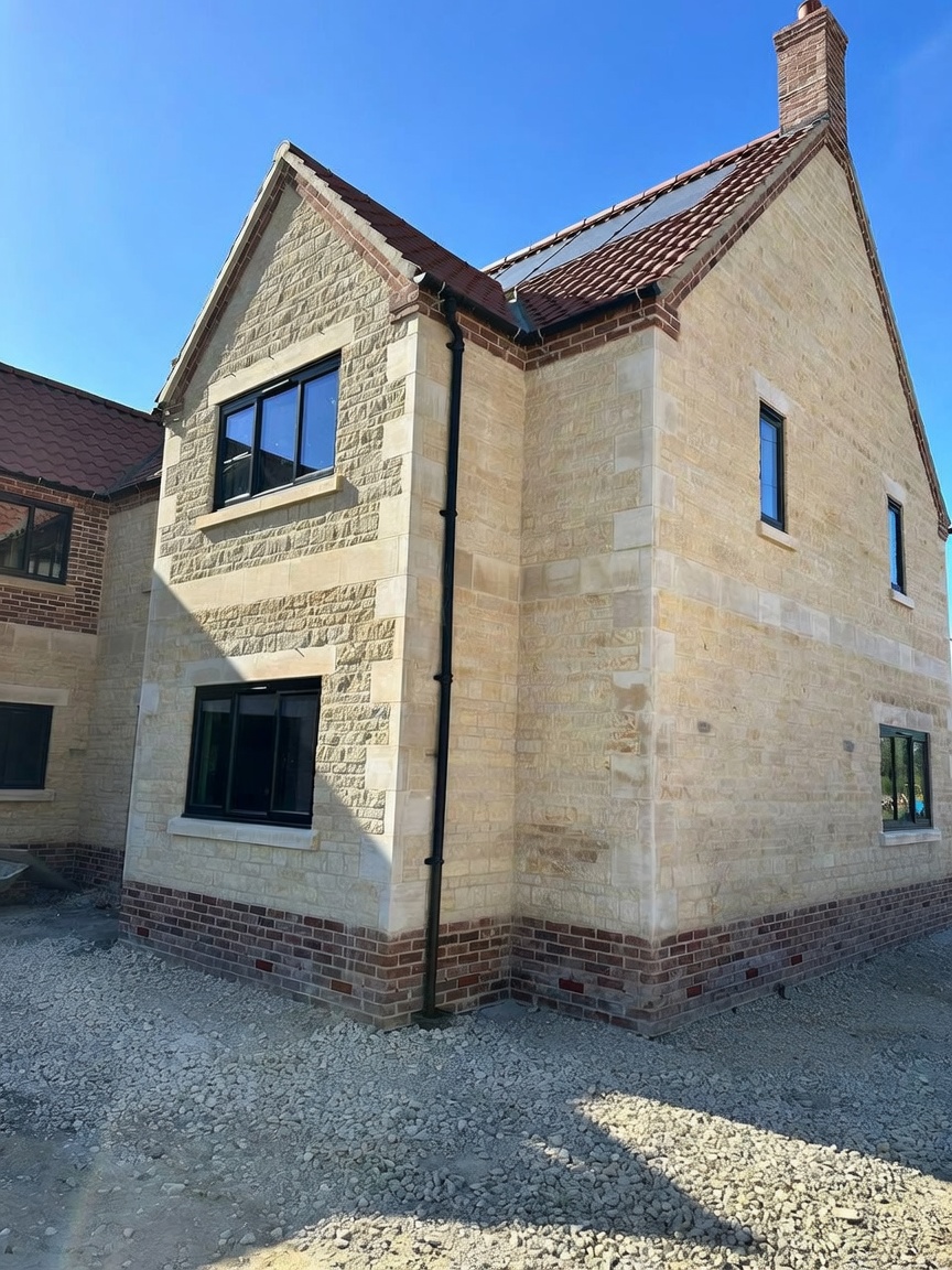 Newly built stone house faced in rock-faced and coursed limestone with ashlar quoins, dressed window surrounds and a red brick plinth