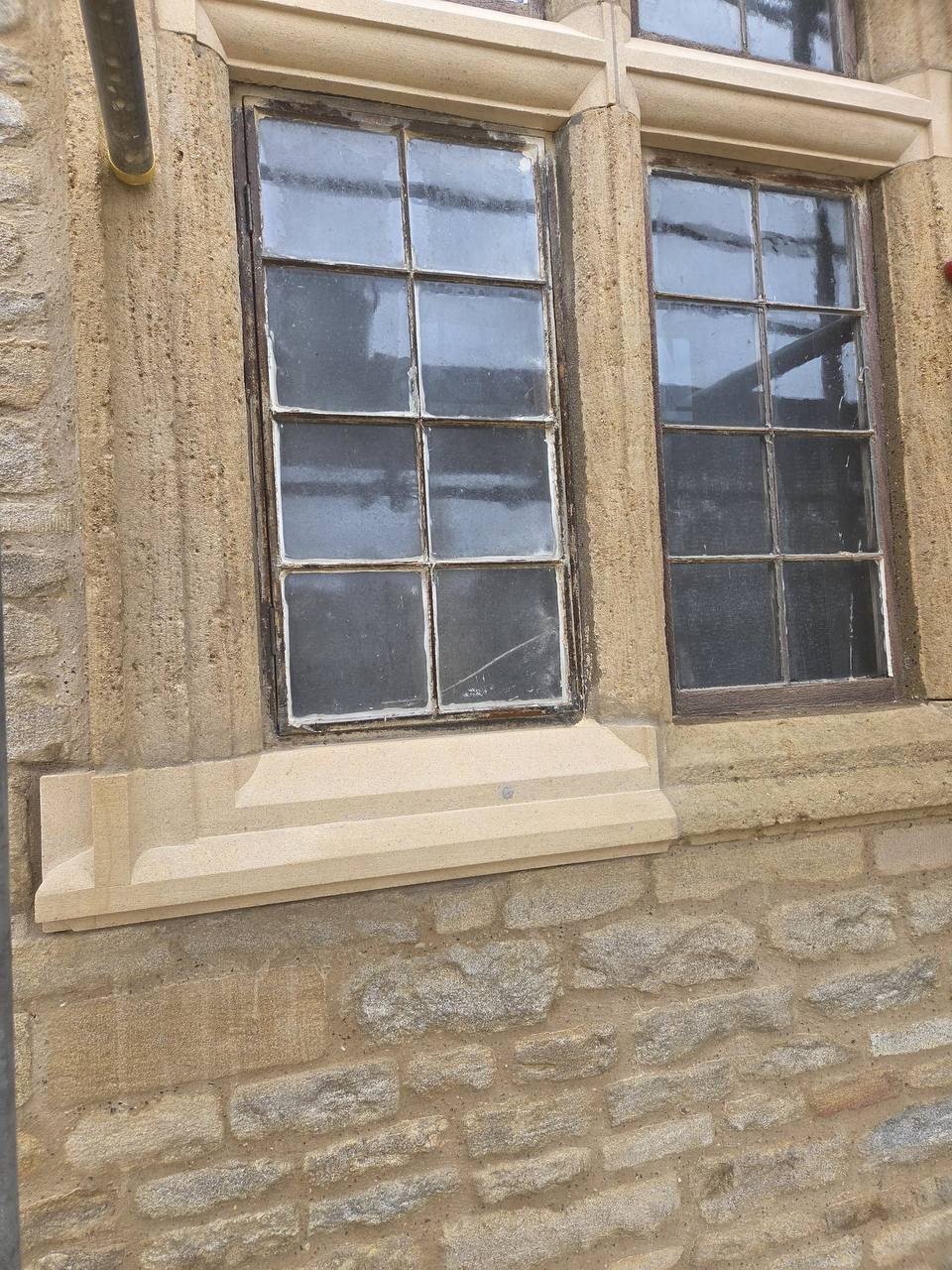 Replacement dressed sandstone cill and window surround fitted beneath timber casements on a coursed rubble stone elevation