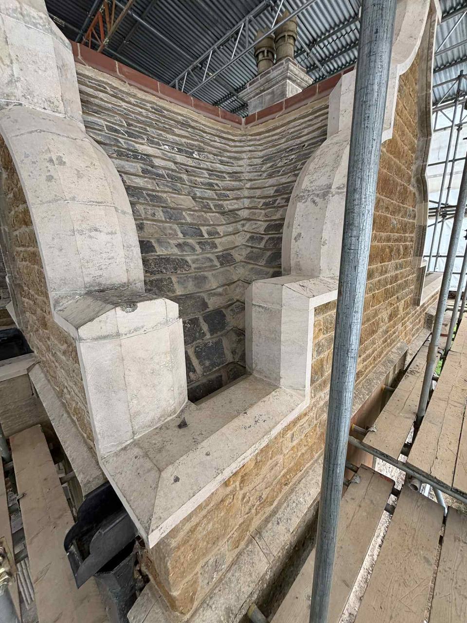 Rebuilt shaped stone gables and parapet with new moulded copings and kneelers flanking a stone-slated roof valley, worked under a temporary scaffold roof