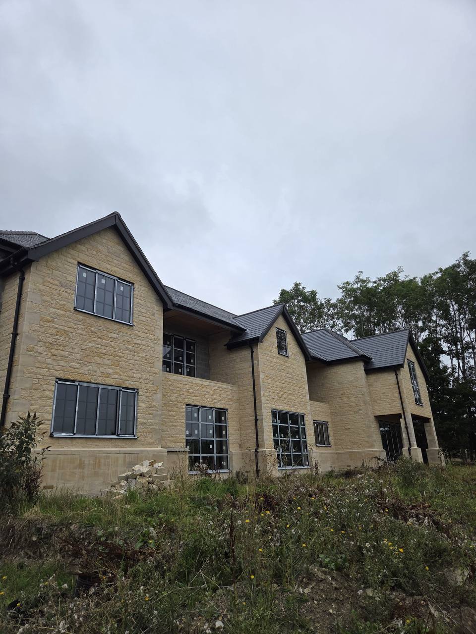 Side elevation of a new build stone house in coursed limestone with ashlar quoins, dressed window surrounds and a run of gables under a slate roof