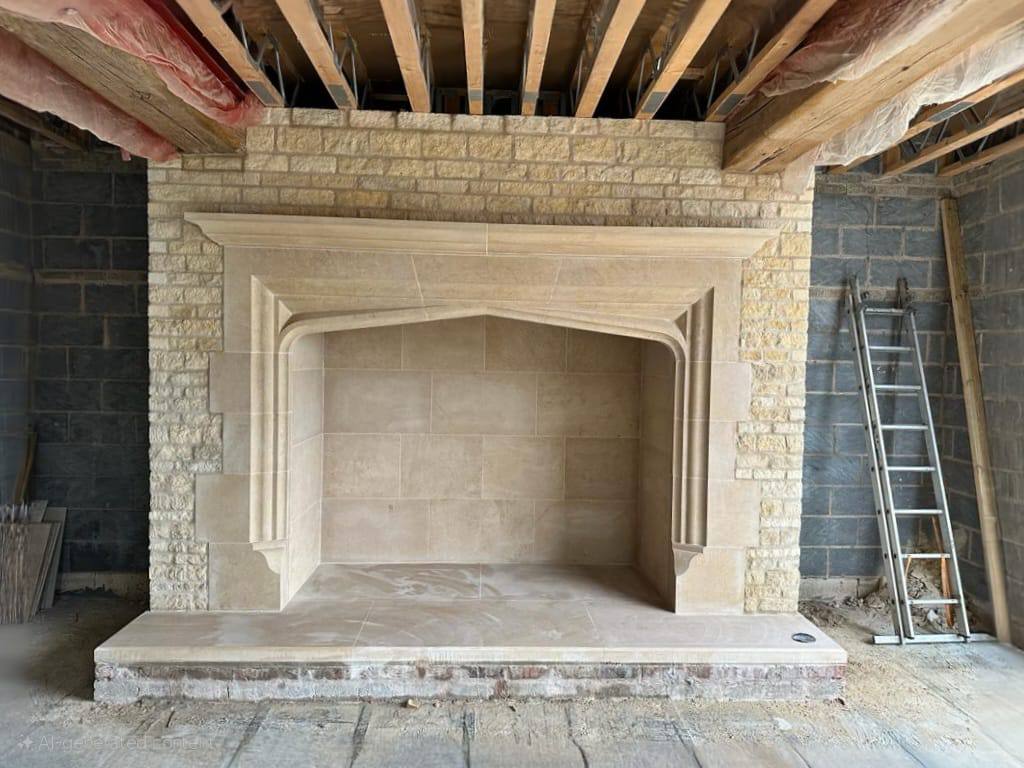 Large hand-carved limestone fireplace with a four-centred arched opening and moulded jambs, newly fitted in a new build house under construction