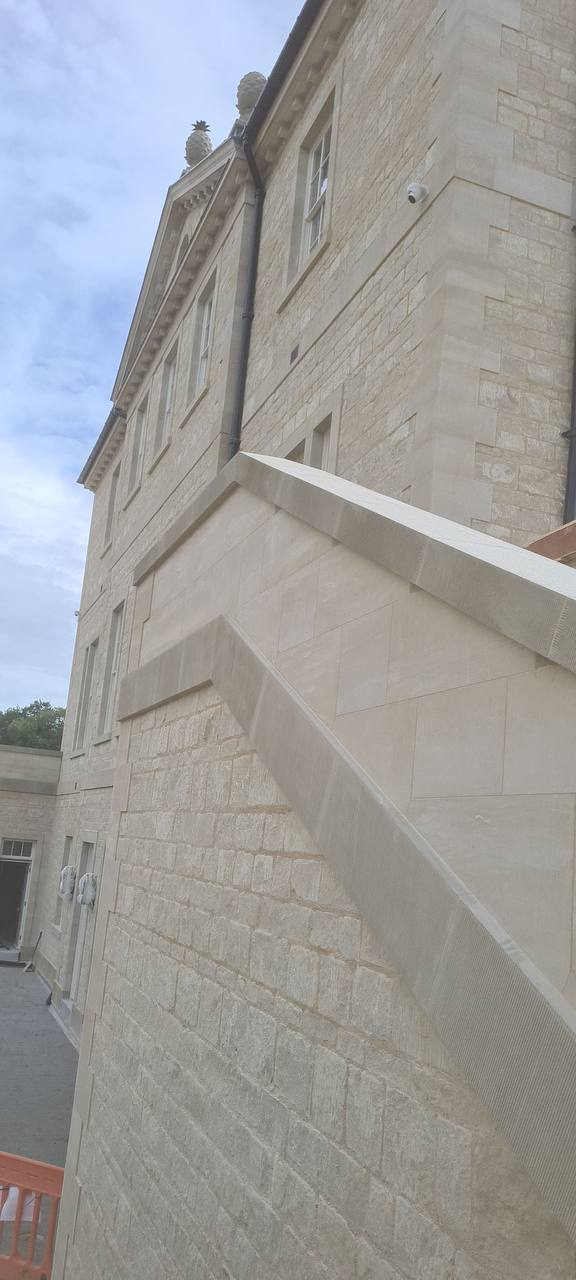 Fine-jointed ashlar limestone elevation of a new country house with a moulded stone cornice, pineapple finials and a rusticated corner